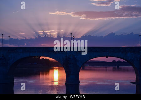 Tramonto mozzafiato con luce proveniente attraverso le nuvole e un colorato sky. In primo piano un ponte di una città in controluce. Foto Stock