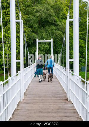 Gli uomini camminare sul fiume Ness passerella di ferro a Ness Isola con uomo che indossa killt con cani Inverness, Scotland, Regno Unito Foto Stock