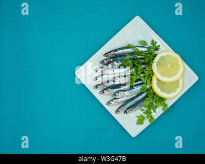 Acciughe fresche in una piastra accompagnato da limone e prezzemolo su uno sfondo blu Foto Stock