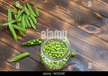 Fresco verde piselli in barattolo di vetro e tutto il baccello scuro su un tavolo di legno. Angolo superiore visualizza lo sfondo con copia spazio. Posto per il testo. Organici naturali home-GRO Foto Stock