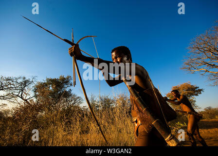 Cacciatori boscimani con arco e frecce che simula una battuta di caccia a Grashoek, Namibia Foto Stock