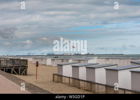 Knokke-Heist, Fiandre, Belgio - 16 Giugno 2019: Knokke-Zoute parte della citta'. Righe di bianco cabine da spiaggia in sabbia con Zeebrugge LNG-sea terminal di Foto Stock
