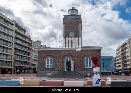 Knokke-Heist, Fiandre, Belgio - 16 Giugno 2019: Knokke-Zoute parte della citta'. Edificio di mattoni con il vecchio faro è l'ufficio del turismo. Statua di candy Foto Stock