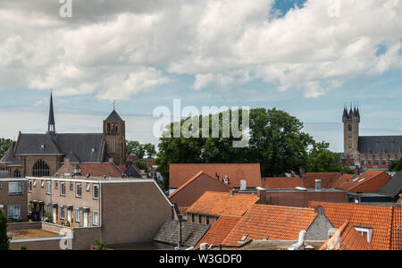 Sluis, Paesi Bassi - 16 Giugno 2019: vista sui tetti rossi a due torri della città sotto il cielo blu con il bianco cloudscape, il verde delle foglie di albero in Foto Stock