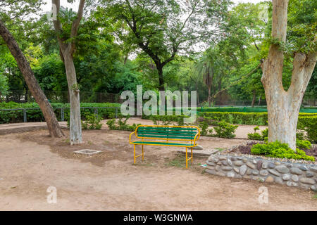 In legno pitturato di rosso e di giallo panchina nel parco giardino sotto gli alberi di ombra. Foto Stock