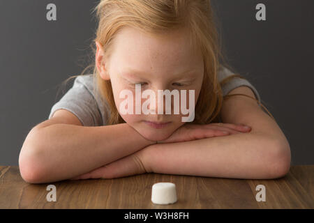 Una giovane ragazza guarda a un singolo marshmallow, tentare la prova di marshmallow Foto Stock