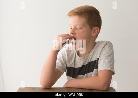 Rosso-testa ragazzo caucasico siede a un tavolo con un unico marshmallow, tentare la prova di marshmallow Foto Stock