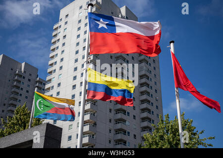 Comore Colombia Cile bandiere. Simboli Nazionali sventolare su pali, Highrise building e cielo blu chiaro sfondo, giornata di sole. Bandiera di Rotterdam parade, Foto Stock