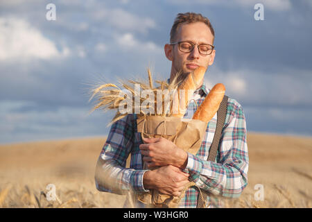 Un uomo sta annusando il pane fresco in piedi in un campo di segale. Foto Stock