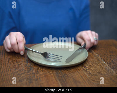 Una donna seduta al tavolo da pranzo in attesa di cibo, la profondità di campo Foto Stock