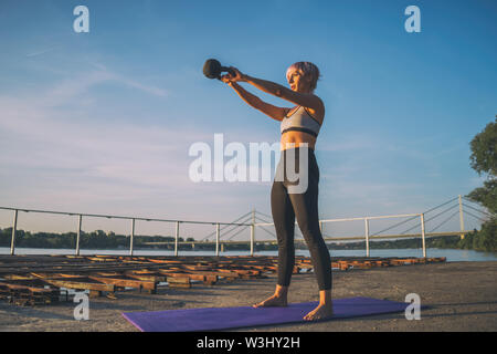 Donna pratica kettlebell pilates sulla giornata di sole. Foto Stock