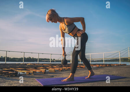 Donna pratica kettlebell pilates sulla giornata di sole. Foto Stock
