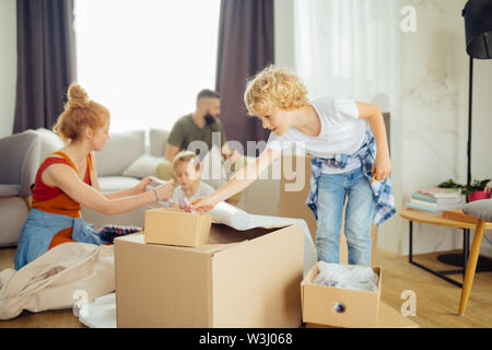 Scatole di cartone. Piacevole ragazzo carino prendendo qualcosa dalla scatola e contribuendo al contempo a disimballare Foto Stock