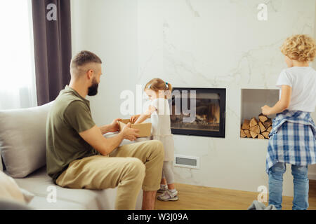 Voler aiutare. Ragazza giovane e carina in piedi vicino al suo padre mentre prendere le cose al di fuori della scatola Foto Stock