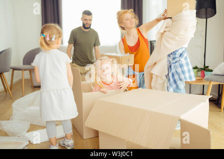 Nella nuova casa. Felice bella ragazza seduta in una casella vuota mentre aiuta i suoi genitori per disimballare le cose Foto Stock