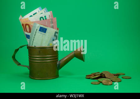 Le banconote in euro assortiti di denominazioni in rame di un annaffiatoio con monete sparse sul verde con copia spazio per temi finanziari Foto Stock