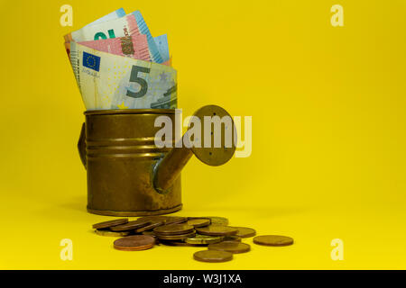 Le banconote in euro assortiti di denominazioni in rame di un annaffiatoio con monete sparse su giallo con copia spazio per temi finanziari Foto Stock