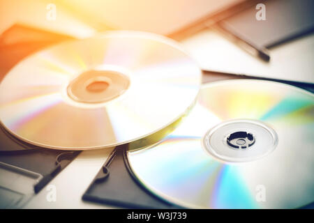 Nuovo CD con musiche giacciono su un tavolo bianco tra le scatole nere per dischi e bagliore con differenti colori luminosi dal sole. Foto Stock