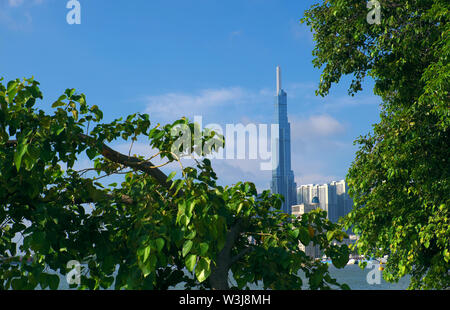 Paesaggio di punto di riferimento 81 vista da Thanh Da, in mattinata con foglie verdi in primo piano sotto il cielo blu, impressione con il più alto edificio in Vietnam Foto Stock