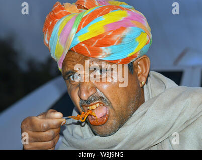 Anziani uomo indiano con un colorato turbante di Rajasthani (pagari) mangia un piatto di spaghetti fritti presso il locale mercato notturno. Foto Stock