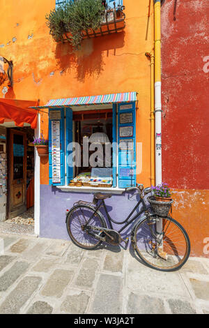 Rusty donna vintage di biciclette parcheggiate fuori un arancio brillante e malva dipinto souvenir shop a Burano, una piccola isola nella laguna di Venezia, Venezia, Italia Foto Stock