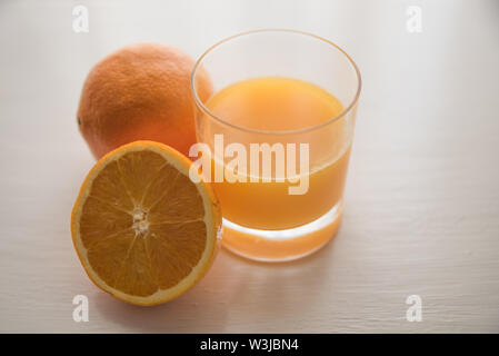 Arance con un bicchiere di succo di arancia su un tavolo bianco sullo sfondo Foto Stock