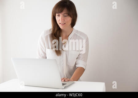Bruna giovane donna con difficoltà tecniche con il suo computer portatile in ufficio Foto Stock
