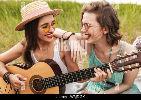 Due ragazze allegro amici di relax all'aperto, suonare la chitarra Foto Stock