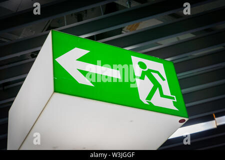 Emergency fire exit segno verde brillante in oscurati background in aeroporto Foto Stock