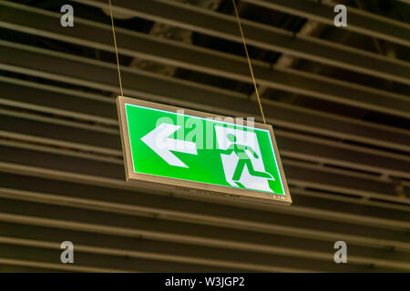 Emergency fire exit segno verde brillante in oscurati background in aeroporto Foto Stock