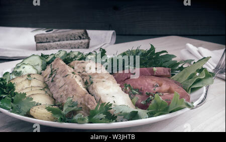 Sul tavolo su una piastra due fette di pesce fritto e patatine fritte, cetrioli , pomodori, insalata, il prezzemolo e l'aneto. Foto Stock