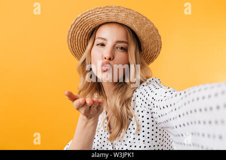 Giovane e bella donna bionda che indossa abiti estivi in piedi isolato su sfondo giallo, prendendo un selfie, invio di kiss Foto Stock