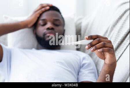 Malati uomo nero nel controllo della sua temperatura a home Foto Stock