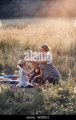 Famiglia di trascorrere del tempo insieme su un prato, vicino alla natura, i genitori e i bambini che giocano insieme, rendendo coronet di fiori selvatici. Candide persone, real Foto Stock