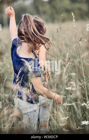 Poco felice ragazza giocando in un'erba alta in campagna. Candide persone, veri momenti e situazioni reali Foto Stock