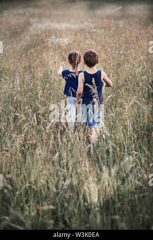 Poco felici i bambini giocando in un'erba alta in campagna. Candide persone, veri momenti e situazioni reali Foto Stock