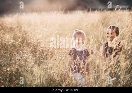 Poco sorridenti i bambini giocando in un'erba alta in campagna. Candide persone, veri momenti e situazioni reali Foto Stock