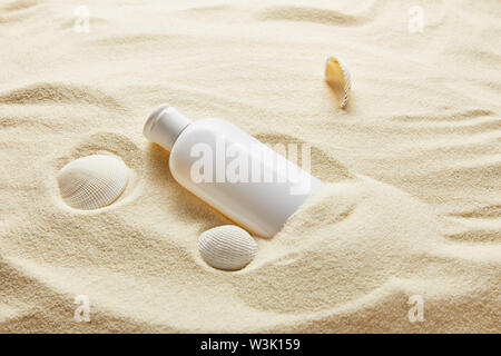 Protezione solare lozione idratante in bottiglia bianca in sabbia con conchiglie Foto Stock