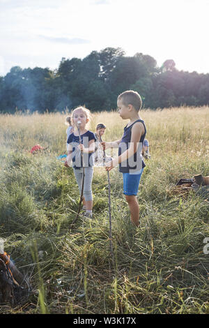 I bambini a mangiare una marshmallows dopo la tostatura di essi su un accampamento su un prato. Candide persone, veri momenti e situazioni reali Foto Stock