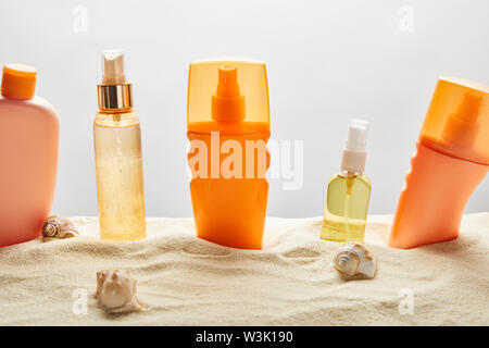 Diversi prodotti per la protezione solare in bottiglie di sabbia con conchiglie su sfondo grigio Foto Stock