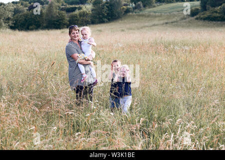 Madre di trascorrere del tempo con i bambini su un prato, vicino alla natura. Donna e bambino in piedi in un'erba. Contenti i bambini a fare ritratti. Candide persone, real mome Foto Stock