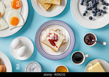 Vista superiore della tabella impostando per la prima colazione e toast con marmellata su piastre su sfondo blu Foto Stock