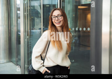 Immagine di una giovane e bella happy business donna posa passeggiate all'aperto vicino al centro business di indossare occhiali. Foto Stock