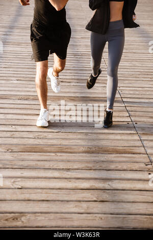 Immagine ritagliata di una sportiva giovane coppia fitness di indossare abbigliamento sportivo insieme per fare jogging sulla spiaggia Foto Stock