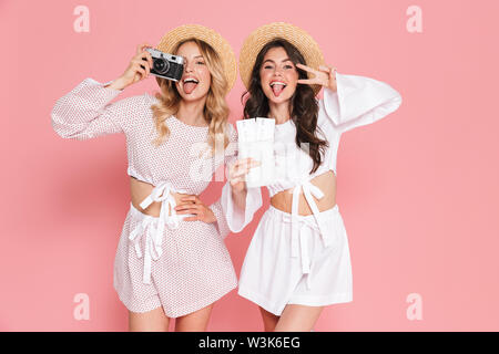 Immagine di entusiasti felice giovani donne belle amici in posa isolate su rosa sfondo parete tenere la fotocamera a fotografare, passaporto con i biglietti. Foto Stock