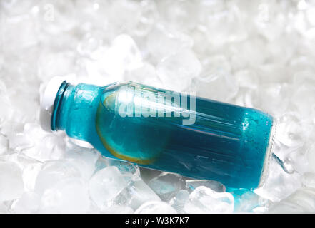 Blu acqua detox con spicchi di limone in una bottiglia di vetro su ghiaccio Foto Stock