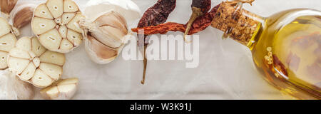 Panoramica di spicchi di aglio, peperoncino essiccato peperoni e bottiglia di olio sul libro bianco sullo sfondo Foto Stock