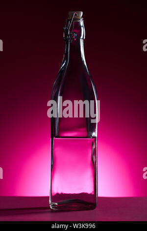 Bottiglia trasparente con acqua su sfondo rosa con retro illuminazione Foto Stock