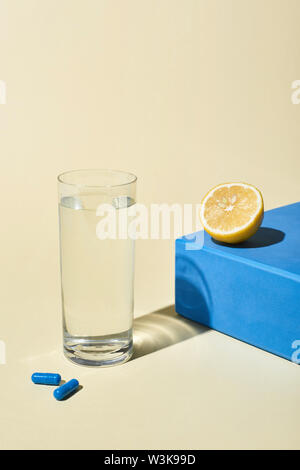 Bicchiere di acqua, blu pillole e metà limone sul cubo blu su sfondo beige Foto Stock