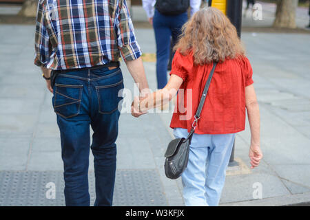 Vecchia coppia tenendo la mano a camminare sulla strada Foto Stock